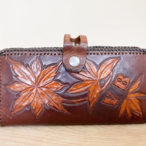 May include: A brown leather wallet with a tooled design of maple leaves and the initials "VB".