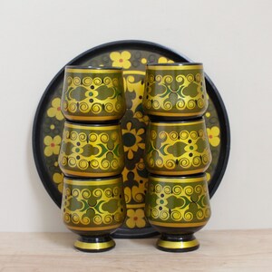 May include: Set of six green and gold ceramic cups with a floral pattern stacked on a black tray.