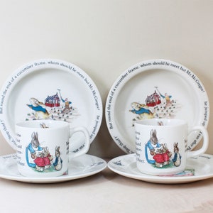 May include: A set of Peter Rabbit themed children's dishes, including two teacups, two saucers, and two plates. The dishes feature a white background with a blue border and a colorful illustration of Peter Rabbit and his siblings. The text on the plates reads "But round the end of a cucumber frame, whom should be met but Mr. McGregor!"