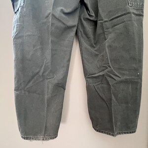 Może przedstawiać: Spodnie cargo w ciemnozielonym kolorze z wieloma kieszeniami. Spodnie wykonane są z wytrzymałej bawełny.