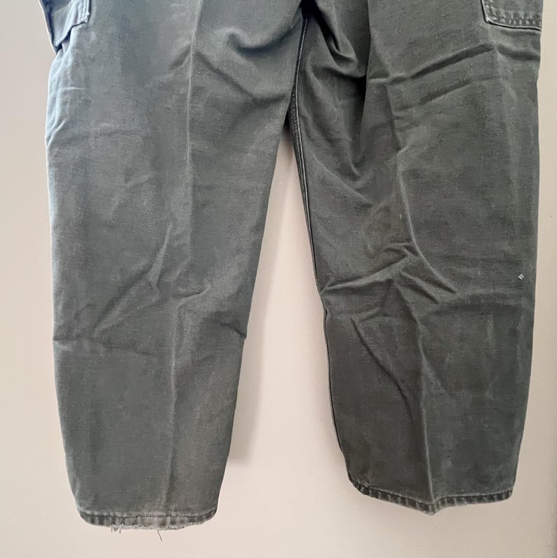 Może przedstawiać: Spodnie cargo w ciemnozielonym kolorze z wieloma kieszeniami. Spodnie wykonane są z wytrzymałej bawełny.