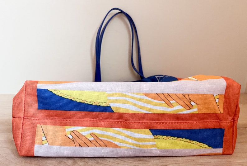 May include: A large orange tote bag with a blue and white striped pattern and a yellow rope design. The bag has two blue handles.