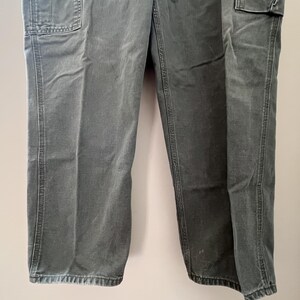 Może przedstawiać: Spodnie robocze w ciemnozielonym kolorze z dwoma dużymi kieszeniami z przodu i dwoma dużymi kieszeniami z tyłu. Spodnie mają prosty kr&oacute;j i luźny fason.