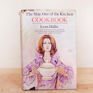 May include: Vintage cookbook titled "The Stay Out of the Kitchen COOKBOOK" by Lynn Dallin. The cover features an illustration of a woman in a purple dress holding a white tureen. The book's title is in red and black.