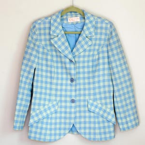 May include: A light blue blazer with a white and light blue checkered pattern. The blazer has a notched collar, three buttons, and two flap pockets.