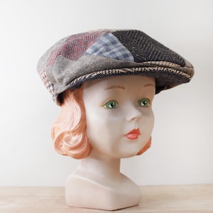 May include: A patchwork newsboy cap with a variety of textured fabrics in shades of gray, brown, and blue. The cap features a classic flat top and a small, curved brim. The cap is displayed on a mannequin head.