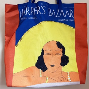 May include: A red, white, and blue tote bag with a vintage Harper's Bazaar magazine cover featuring a woman with dark hair and a yellow hat. The cover reads "Harper's Bazaar" and "January 1932".