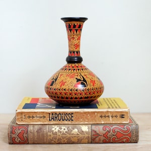 May include: A black and orange ceramic vase with a geometric design. The vase is sitting on top of three books.