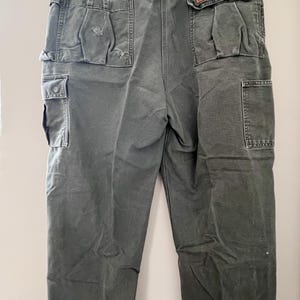 Może przedstawiać: Spodnie cargo w ciemnozielonym kolorze z wieloma kieszeniami. Spodnie mają prosty kr&oacute;j nogawek i luźny fason.