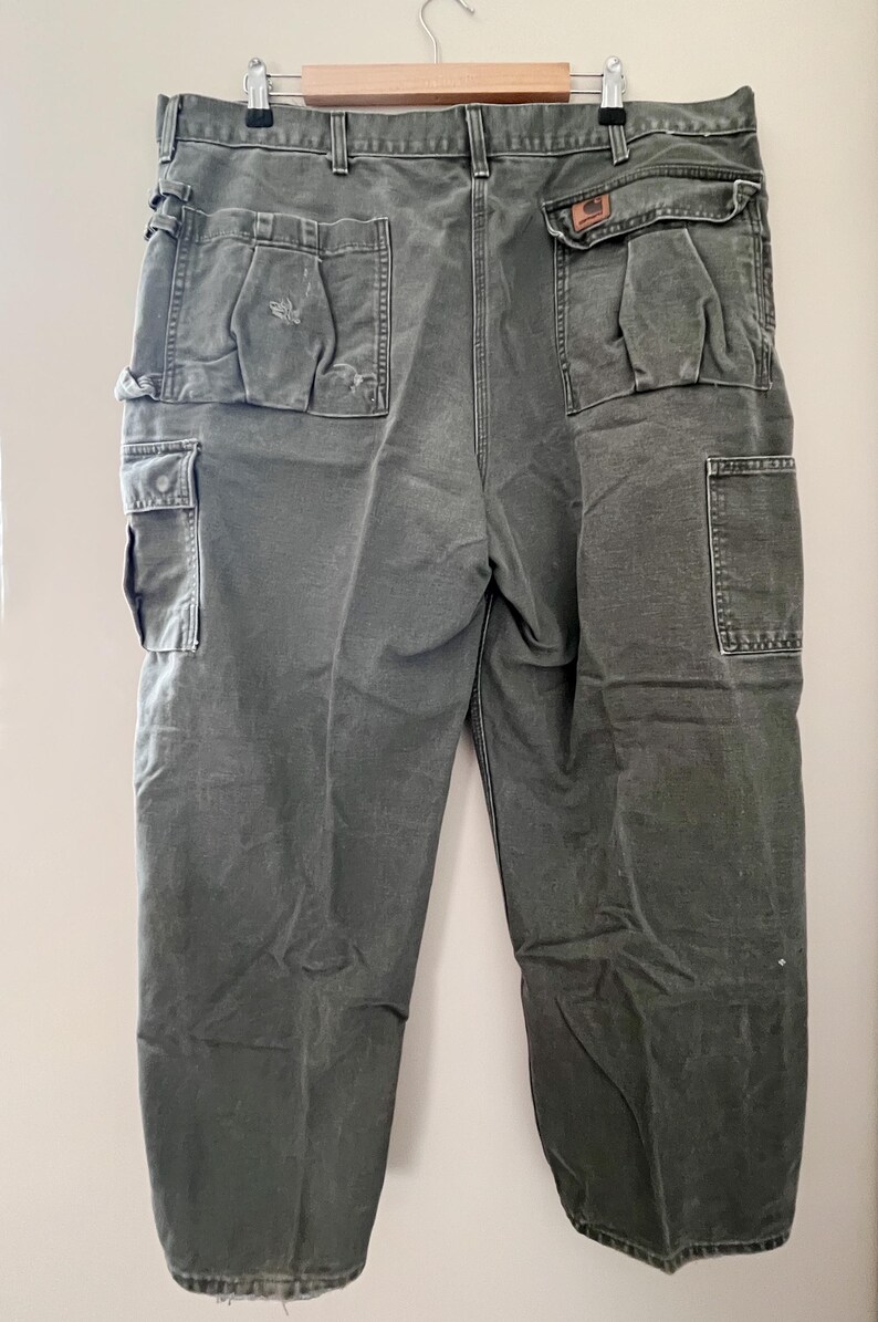 Może przedstawiać: Spodnie cargo w ciemnozielonym kolorze z wieloma kieszeniami. Spodnie mają prosty kr&oacute;j nogawek i luźny fason.