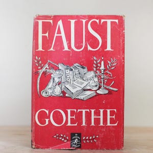May include: A red book cover with the title "FAUST GOETHE" in white lettering. The cover features a black and white illustration of an hourglass, books, a skull, and a candle.