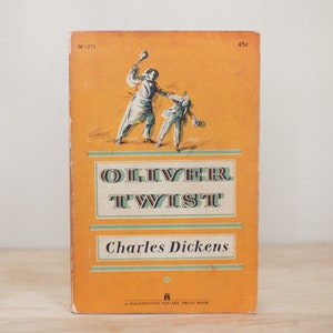 May include: A vintage paperback book cover with an orange background. The cover features a black and white illustration of two figures, one holding a spoon and the other holding a bowl. The title of the book is "Oliver Twist" by Charles Dickens. The book is a Washington Square Press book.