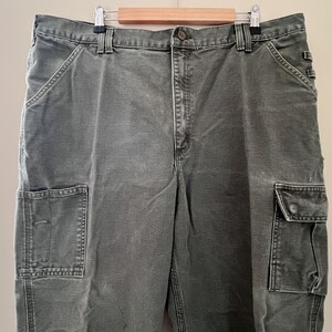 Może przedstawiać: Spodnie cargo w ciemnozielonym kolorze z wieloma kieszeniami.