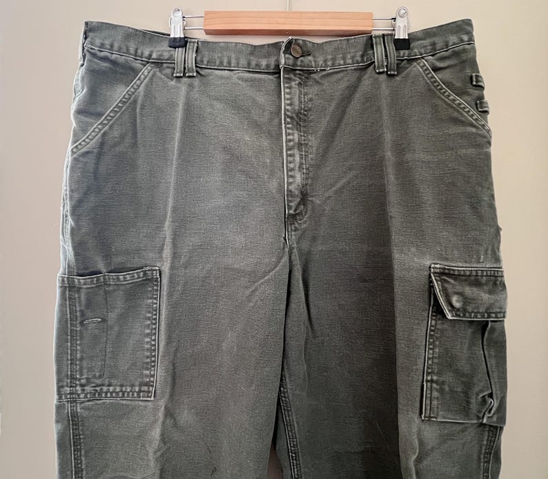 Może przedstawiać: Spodnie cargo w ciemnozielonym kolorze z wieloma kieszeniami.