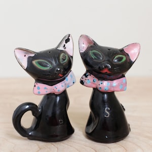 May include: A pair of black ceramic cat salt and pepper shakers with pink and blue polka dot bow ties. The salt shaker is labeled "S" and the pepper shaker is labeled "P".