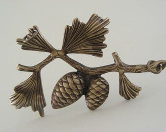 May include: A bronze pendant featuring a stylised pine branch with two pine cones and a loop for hanging.