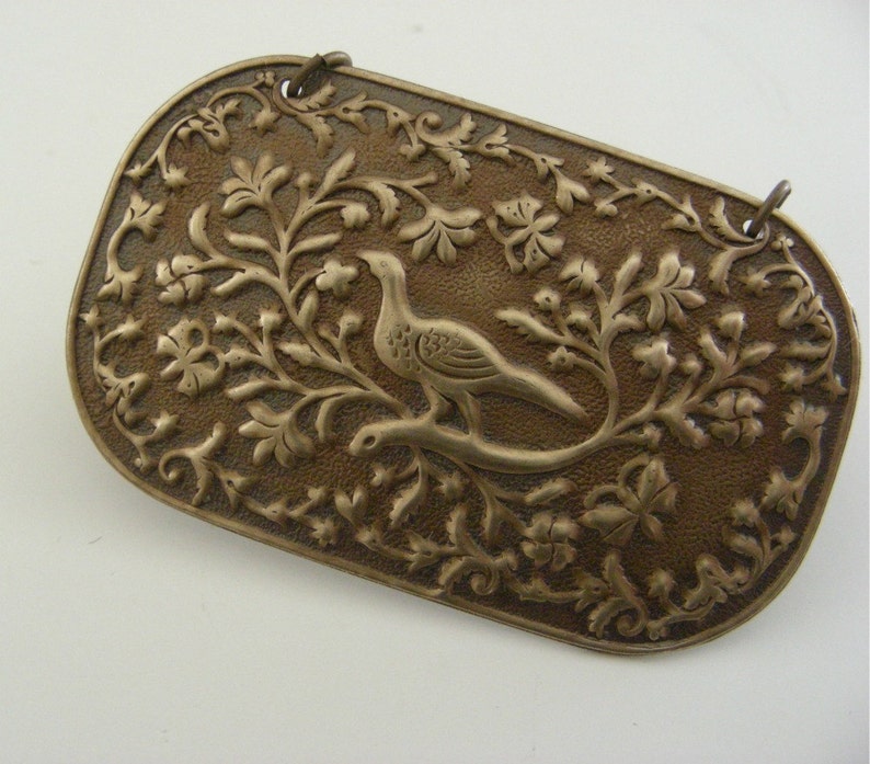 May include: A silver-toned metal plaque with an intricate design of a bird perched on a branch surrounded by leaves and flowers.