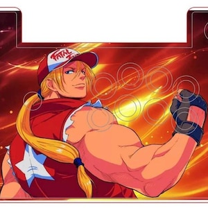 May include: An arcade control panel featuring a character from the video game "Fatal Fury". The character is a muscular man with blonde hair and a red and white shirt. The background is a fiery orange and yellow.