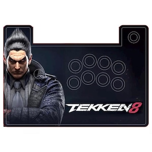Puede incluir: Un stick de lucha de arcade negro y rojo con un logotipo de Tekken 8 y un personaje del juego. El stick de lucha tiene ocho botones y una palanca de mando.
