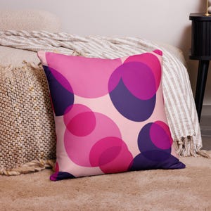 May include: A pink and purple throw pillow with a geometric pattern of overlapping circles. The pillow is made of soft fabric and has a subtle sheen.