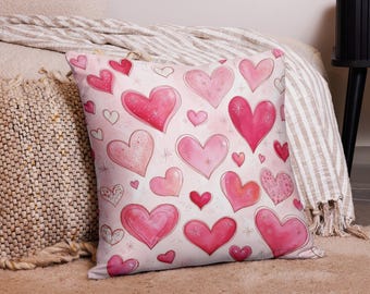 May include: A pink and white cushion with a pattern of pink hearts of different sizes. The hearts have a watercolour look and some have glitter accents.