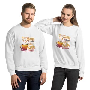 Puede incluir: Sudaderas blancas con el texto "May Your Coffee Be Strong & Your Faith Stronger" en naranja y amarillo. El diseño incluye una taza de café. Las sudaderas son usadas por un hombre y una mujer.
