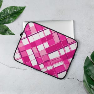 May include: A laptop sleeve with a vibrant geometric pattern in shades of pink and white. The sleeve has a black zipper and a black border. The design features intersecting lines and squares, creating a modern and stylish look. The sleeve is designed to protect a laptop.