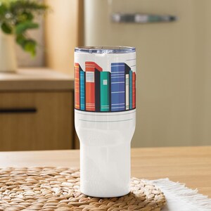 Op de afbeelding: Een witte geïsoleerde beker met een kleurrijke afbeelding van boeken. De boeken zijn in verschillende kleuren, waaronder rood, blauw en groen. De beker heeft een doorzichtig deksel en is ontworpen om dranken warm of koud te houden.