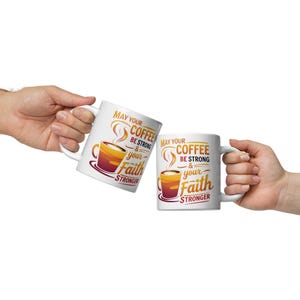 Puede incluir: Dos tazas de café de cerámica blanca con el texto "May your coffee be strong & your faith stronger" en negro y naranja. Cada taza presenta un gráfico de taza de café. Las tazas se sostienen sobre un fondo blanco.