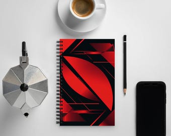 Könnte beinhalten: Ein schwarzes und rotes Spiralnotizbuch mit einem abstrakten geometrischen Design. Das Notizbuch liegt auf einer weißen Oberfläche mit einer Kaffeetasse, einem Bleistift und einem schwarzen Smartphone.