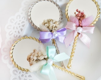 May include: Three small hand mirrors with gold rope-like handles. Each mirror has a different colored bow and dried flowers attached to the handle.