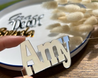May include: A silver mirror acrylic nameplate with the name "Amy" in bold, white lettering. The nameplate is being held by a hand.