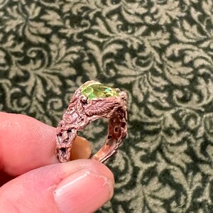 May include: A ring with a green gemstone set in a detailed, intricate, copper band.