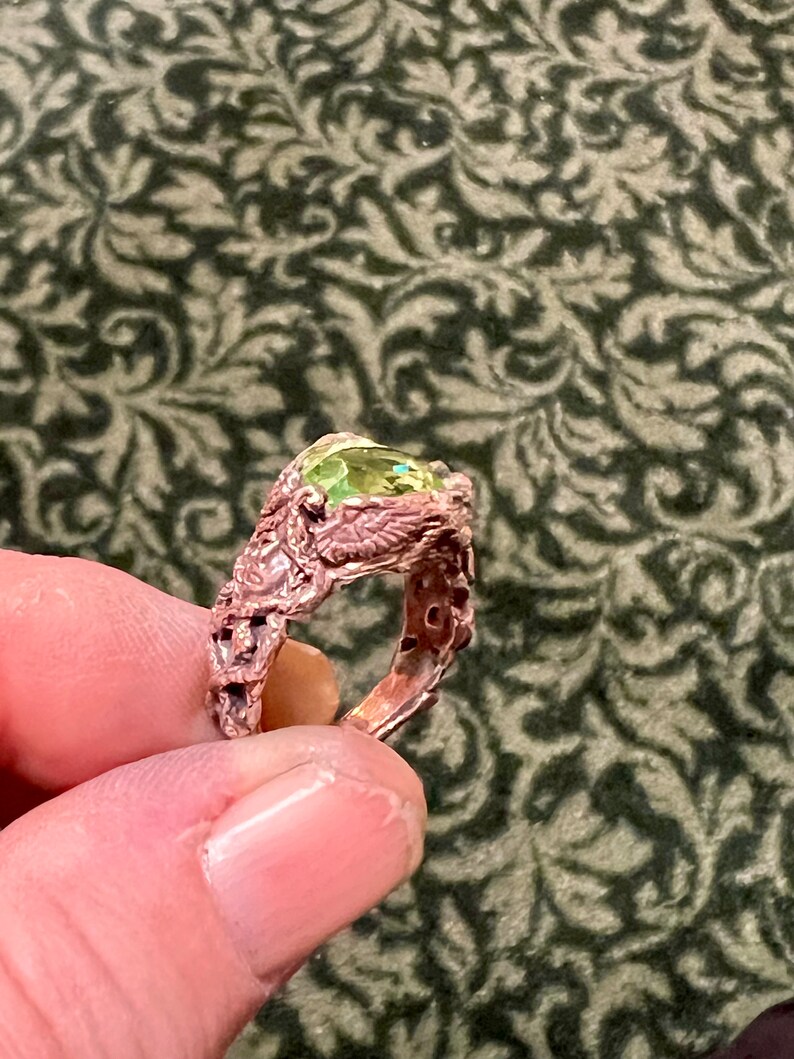 May include: A ring with a green gemstone set in a detailed, intricate, copper band.