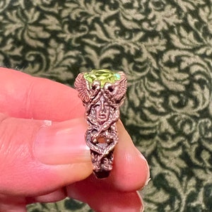 May include: A copper ring with a green gemstone and a detailed design of a winged creature with a human face.