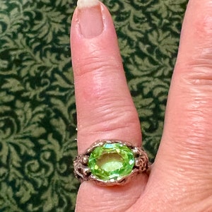 May include: A silver ring with a large, oval-shaped, light green gemstone set in a textured, claw-like setting.