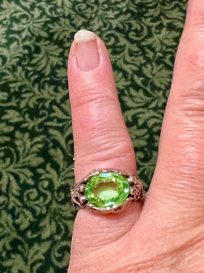 May include: A silver ring with a large, oval-shaped, light green gemstone set in a textured, claw-like setting.