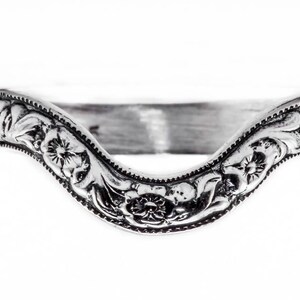 May include: A silver ring with a floral design. The ring is shaped like a V and has a delicate, intricate pattern.