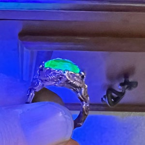 May include: A silver ring with a green gemstone set in a detailed, dragon-like design.