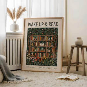 May include: A framed art print featuring the words "WAKE UP & READ" above a colourful illustration of a bookshelf filled with books, plants, and flowers. The print is set against a dark green background and includes the text "NATIONAL LIBRARY WEEK 1951".