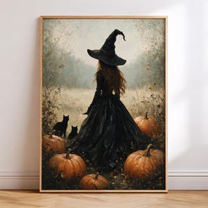 May include: A framed wall art print depicting a figure wearing a black witch hat and a long black dress standing in a field. Two black cats sit near the figure, surrounded by several orange pumpkins in a muted, autumnal landscape setting.