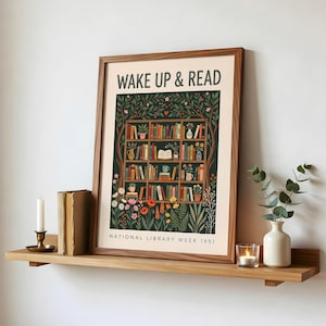 May include: A framed print with the text "WAKE UP & READ" above a detailed illustration of a bookshelf filled with books and plants. The print is on a wooden shelf with a candle, books, and a vase.