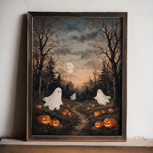 Op de afbeelding: Een ingelijste wandkunstprint met een donker boslandschap bij schemering, inclusief een volle maan, kale bomen en een kronkelend pad. Drie witte spookfiguren zweven boven de grond, die bezaaid is met gloeiende oranje pompoenen.