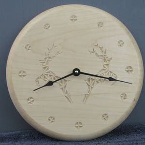 May include: A wooden clock with a carved design of two reindeer. The clock face is made of light wood and has black hands. The clock is surrounded by a circle of small stars.