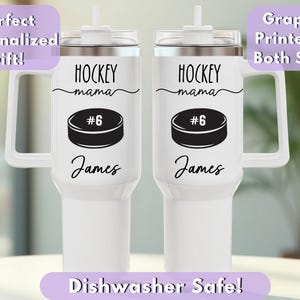 May include: Two white insulated tumblers with handles, featuring a hockey puck graphic with the number 6, the text "HOCKEY mama", and the name "James". The tumblers have a silver rim and a white lid with a straw.