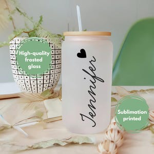 K&ouml;nnte beinhalten: Ein gefrosteter Glasbecher mit Bambusdeckel und Strohhalm. Der Becher hat ein Herz und den Namen "Jennifer" aufgedruckt. Der Becher ist im Sublimationsverfahren bedruckt.