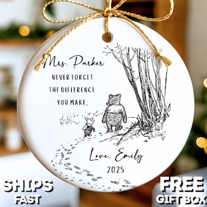 May include: A white ceramic ornament with a gold string for hanging. The ornament features a black and white illustration of Winnie the Pooh and Piglet walking in a forest. Text includes "Mrs. Parker, Never Forget The Difference You Make, Love, Emily, 2025."