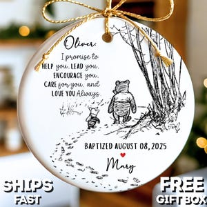 May include: A white ceramic Christmas ornament with a gold ribbon. It features a Winnie the Pooh illustration and text: "Oliver: I promise to help you..." and "Baptized August 08, 2025 Mary."