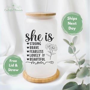 K&ouml;nnte beinhalten: Ein wei&szlig;er, mattierter Glasbecher mit Bambusdeckel und Strohhalm. Der Becher hat eine schwarze Grafik mit dem Text "She is" und einer Liste positiver Eigenschaften sowie dem Wort "mom" am unteren Rand. Die Grafik enth&auml;lt auch einen kleinen Schmetterling und zwei Blumen.