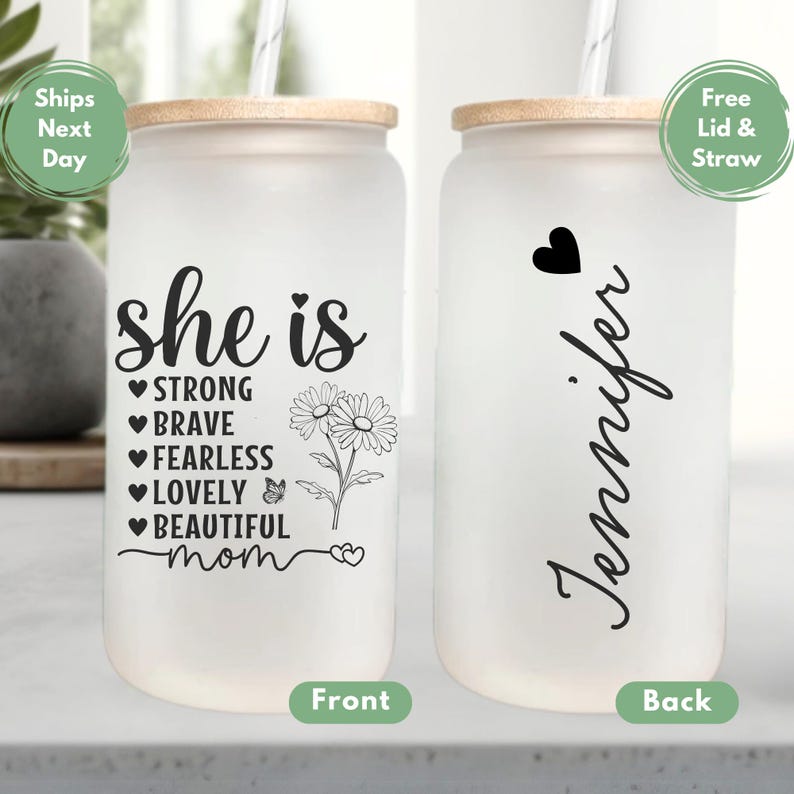 K&ouml;nnte beinhalten: Ein wei&szlig;er, mattierter Glasbecher mit Bambusdeckel und Strohhalm. Die Vorderseite des Bechers zeigt den Text "she is" mit einer Liste positiver Eigenschaften und einem Blumendesign. Die R&uuml;ckseite des Bechers zeigt den Namen "Jennifer" in einer Schreibschrift.